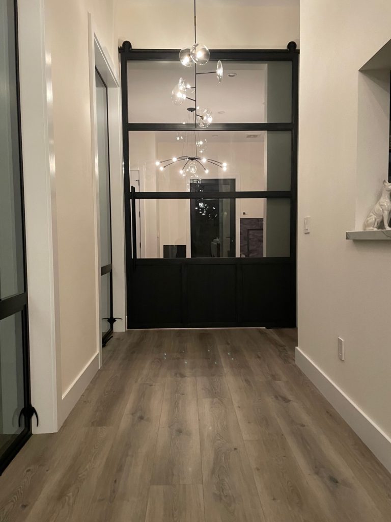 Oversized black steel and glass barn door with a toe kick in a hallway