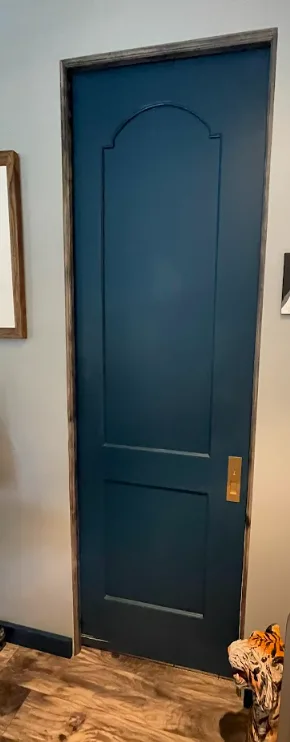 Dark teal painted shaker style pocket door with an arched top panel and brass pull