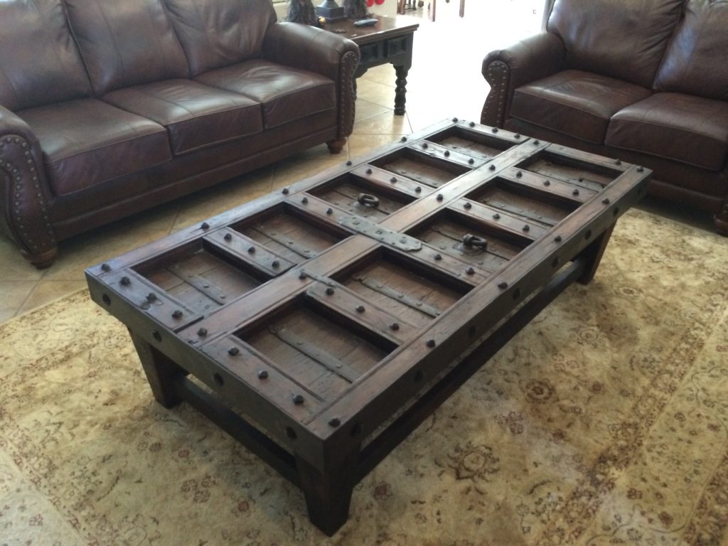 Reclaimed wood door coffee table with metal studs on a dark base between two leather sofas