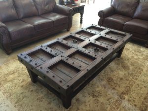 Door Coffee Table Reclaimed wood door coffee table with metal studs on a dark base between two leather sofas