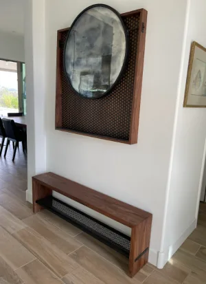 Round antique mirror in a walnut wood frame above a custom walnut wood bench