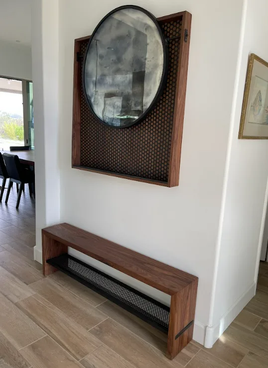Round antique mirror in a walnut wood frame above a custom walnut wood bench