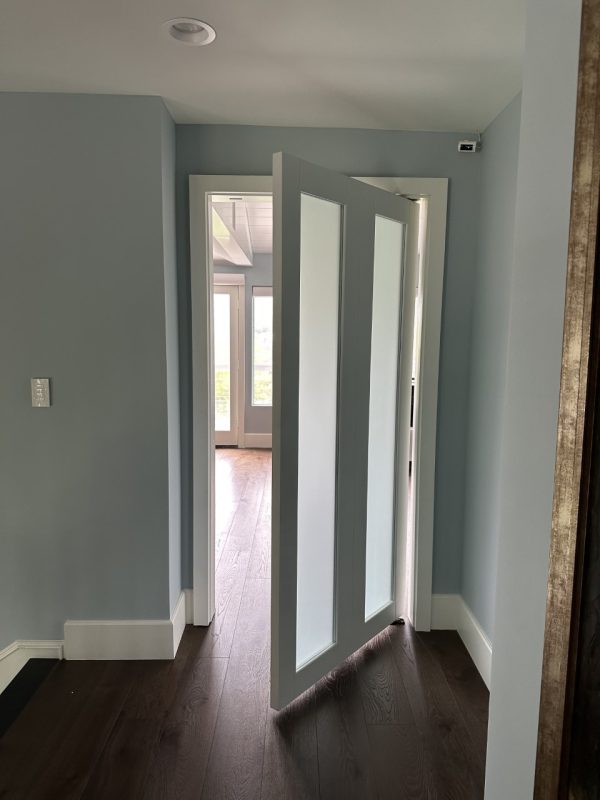 White painted shaker style pivot door with satin glass panels opening into a bedroom