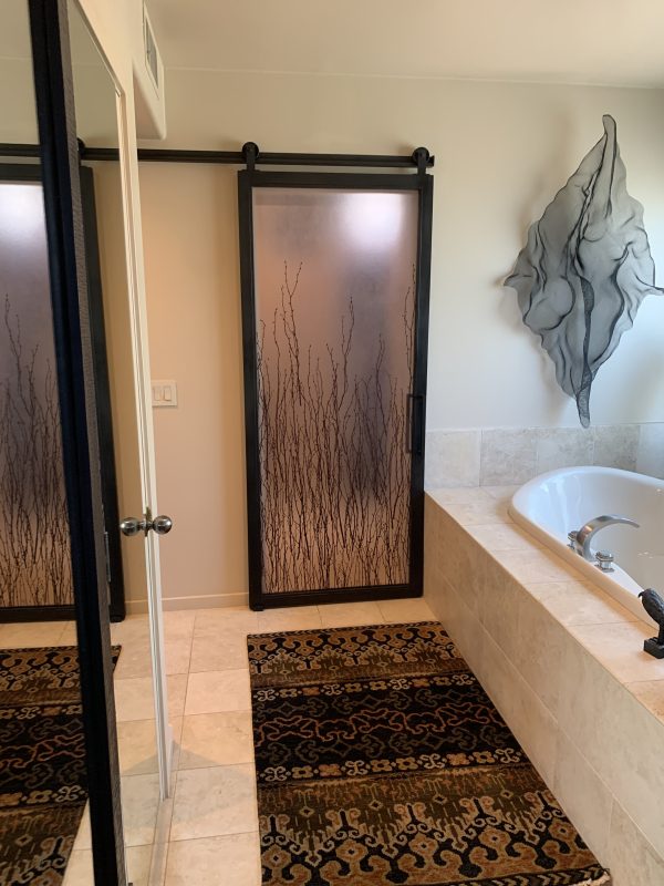 Single 3-Form Birch Panel with Metal Barn Door Metal barn door with a 3form birch branch resin panel in a primary bathroom