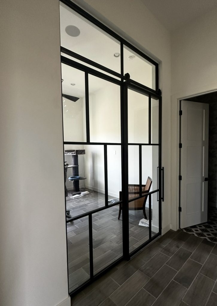 Single black metal and glass barn door with a fixed panel and transom