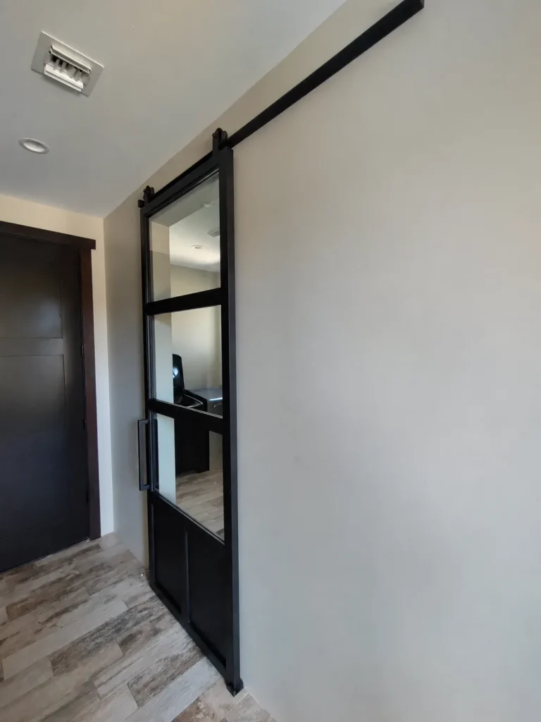 Narrow single black metal and glass barn door with a solid lower panel
