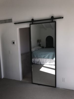 Single Mirror with Steel Frame Single mirror barn door in a thin black steel frame at a bedroom entry