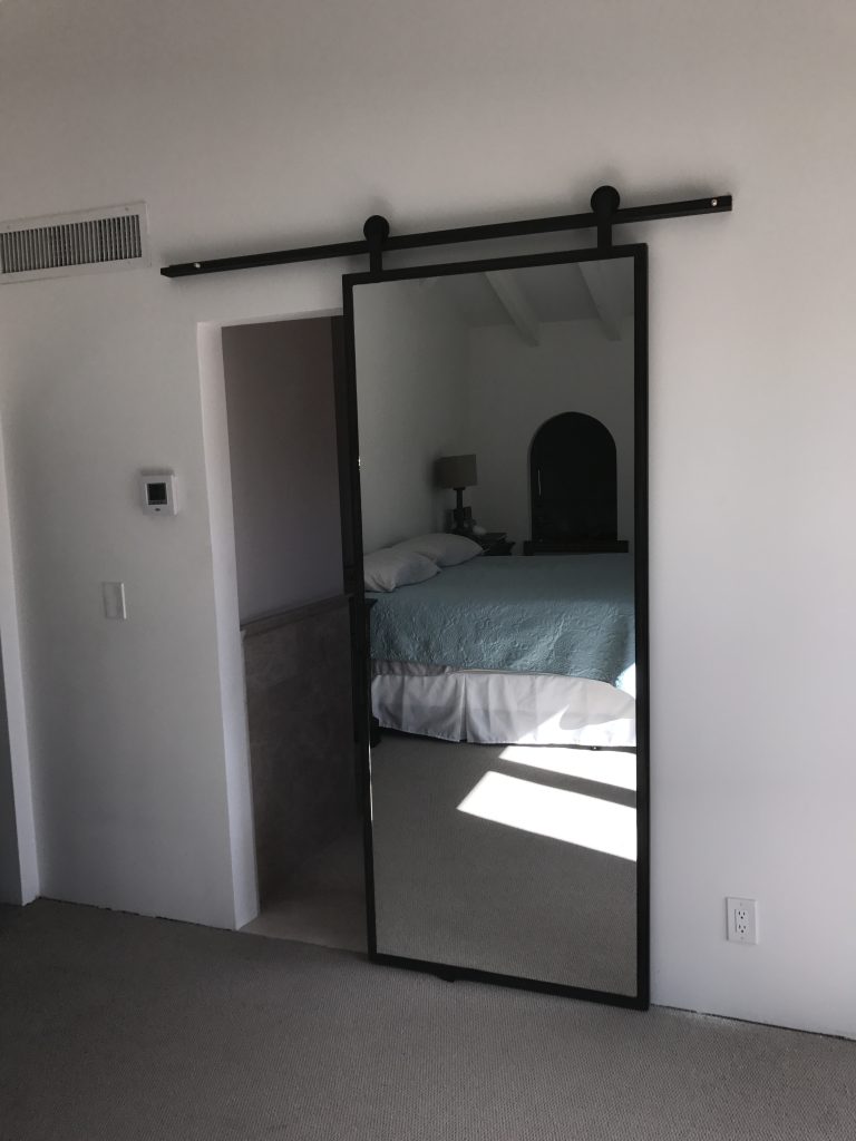 Single mirror barn door in a thin black steel frame at a bedroom entry