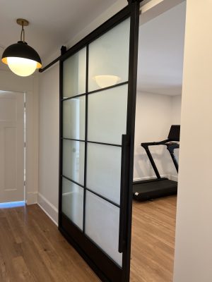Single Steel and Frosted Glass Barn Door Single black steel barn door with frosted glass panels next to a home gym