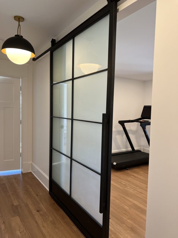 Single black steel barn door with frosted glass panels next to a home gym