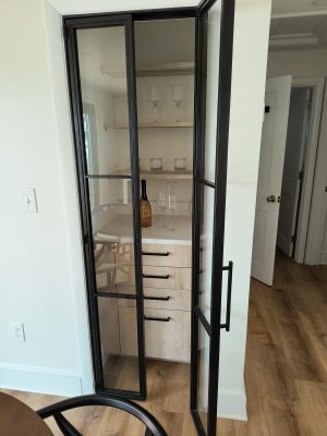 Narrow black metal and glass hinged pantry door opening to pantry shelves