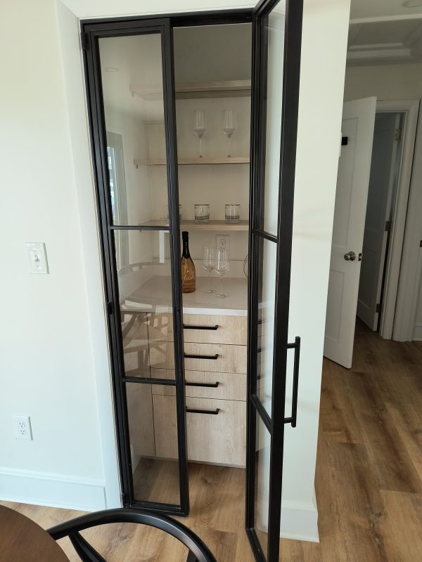 Narrow black metal and glass hinged pantry door opening to pantry shelves
