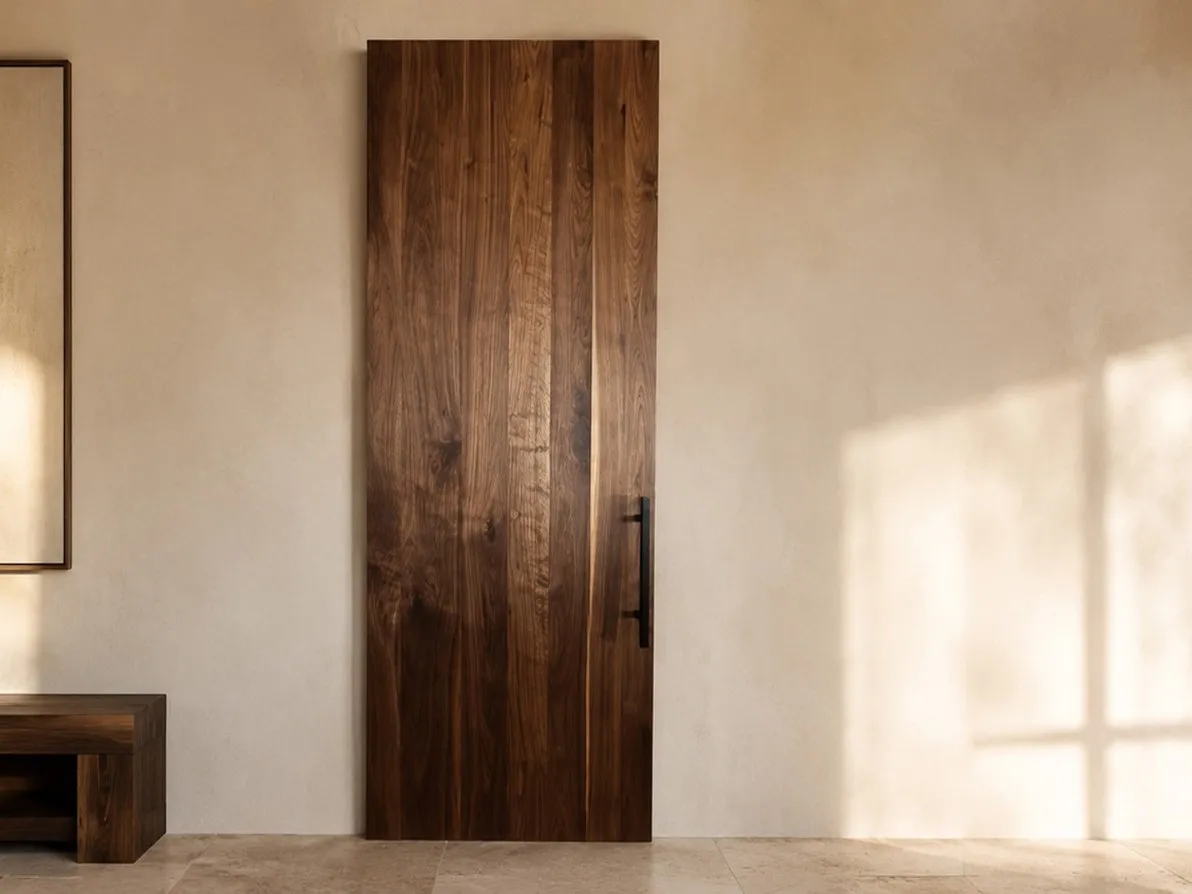 Solid walnut sliding door with a black pull handle and concealed hardware in a warm plaster-walled room