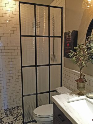 Black steel and reeded glass divider in a tiled bathroom