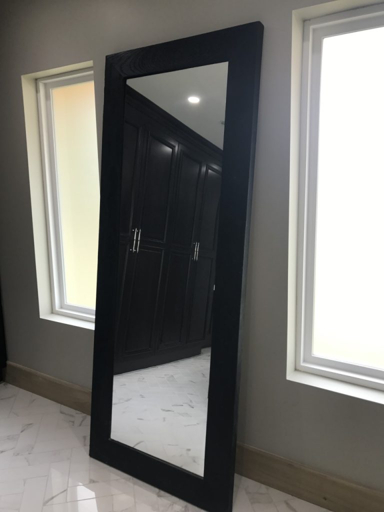Wood framed full length mirror next to windows