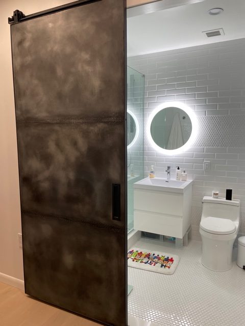Patina zinc panel sliding barn door opening to a bright white bathroom