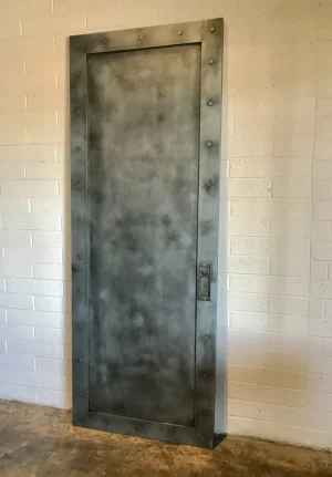 Zinc pocket door with a riveted frame and a recessed flush pull handle against a white brick wall